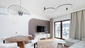 Una sala de estar moderna con una mesa de comedor de madera, sillas blancas, un sofá y un televisor sobre un mueble blanco.