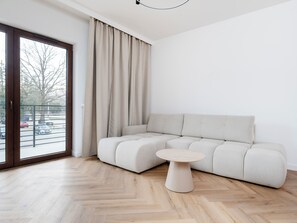 A modern living room with a sectional sofa, a round coffee table, and a large window with curtains. - Stawy Jana Harmony Apartment (Łódź)