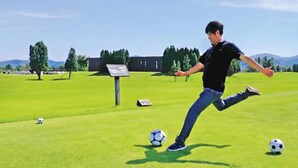 Une personne qui joue au football sur un terrain enherbé, sous un ciel dégagé.