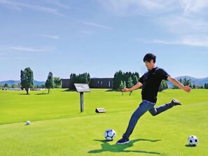 A person playing soccer on a grassy field with a clear sky.