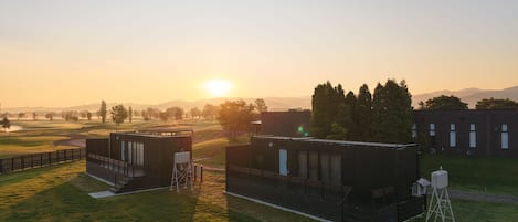A grassy area with buildings, a clear sky, and a setting sun.