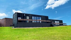 Un bâtiment moderne doté de grandes fenêtres et d’un toit plat, situé sur une colline verdoyante.
