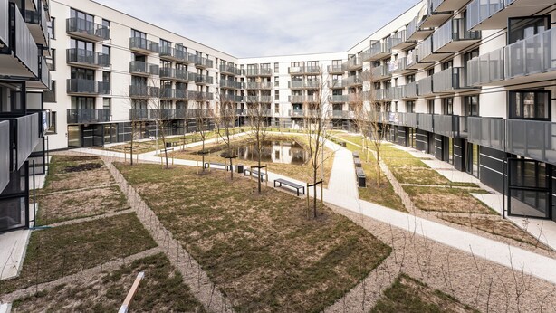 Een modern appartementencomplex met meerdere balkons, een centrale binnenplaats met een klein vijvertje en een verzorgd gazon.