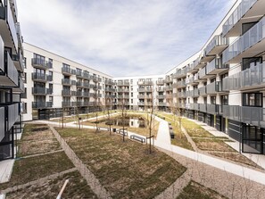 Ein moderner Wohnkomplex mit mehreren Balkonen, einem zentralen Innenhof mit einem kleinen Teich und einem gepflegten Rasen.