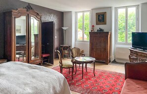 Ein Zimmer mit einem Bett, einem Schreibtisch, einem Sessel, einem Fernseher und einem großen Spiegel.