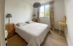 Ein Schlafzimmer mit einem Bett, zwei Nachttischen, einer Lampe, einem Spiegel und einem Fenster mit Vorhängen.