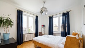 Ett sovrum med en säng i trä, en krukväxt, ett element och ett fönster med gardiner.