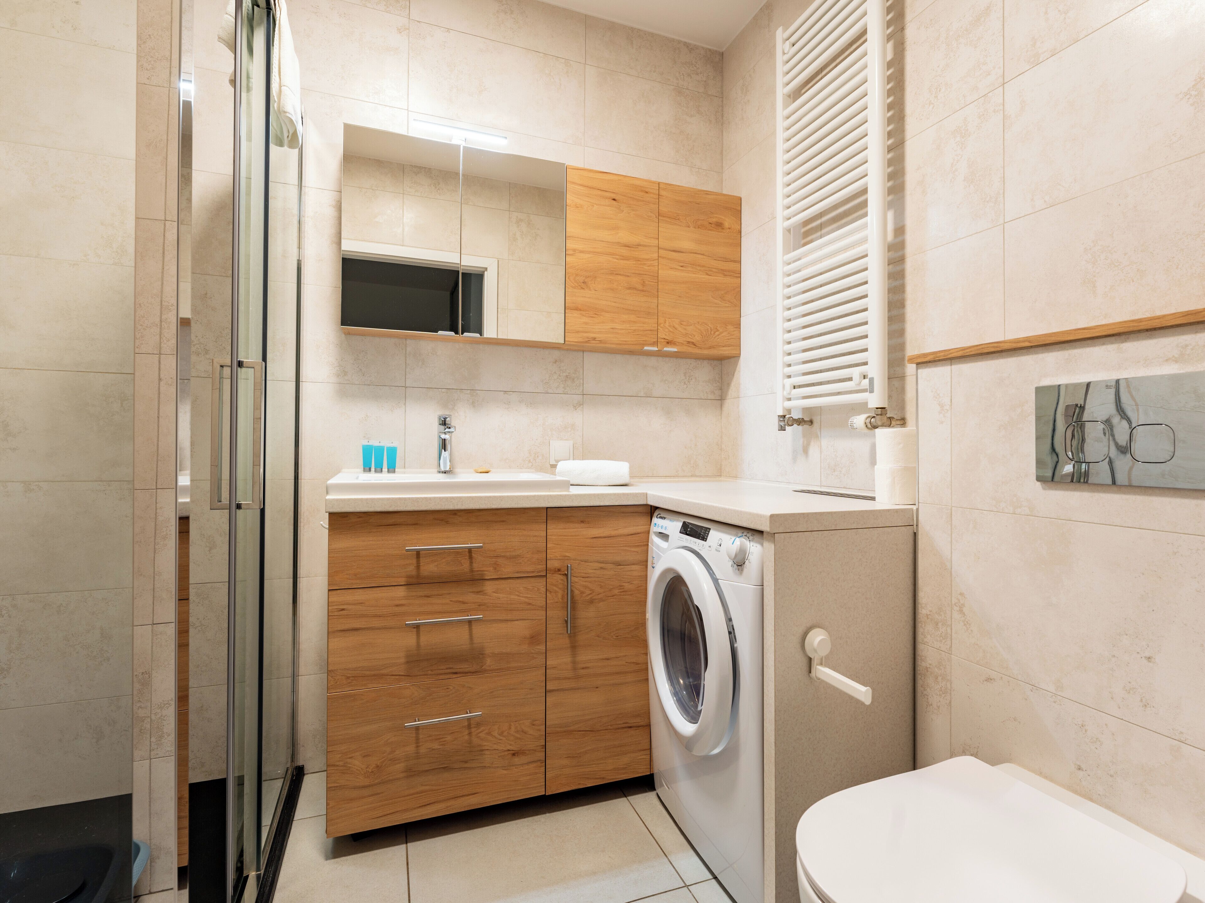 Un baño moderno con cabina de ducha de vidrio, muebles de madera, lavadora integrada y un inodoro.