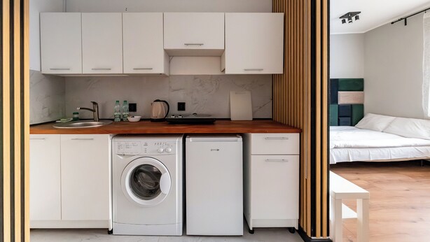 A compact kitchen with a washing machine, a small refrigerator, and white cabinets. - Gdynia Centrum Coastal Studio (Gdynia)