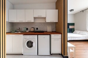 Una cucina compatta con lavatrice, un piccolo frigorifero e mobili bianchi.