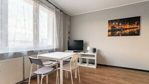 A room with a dining table, chairs, a TV, and a painting on the wall. - Gdynia Centrum Coastal Studio (Gdynia)