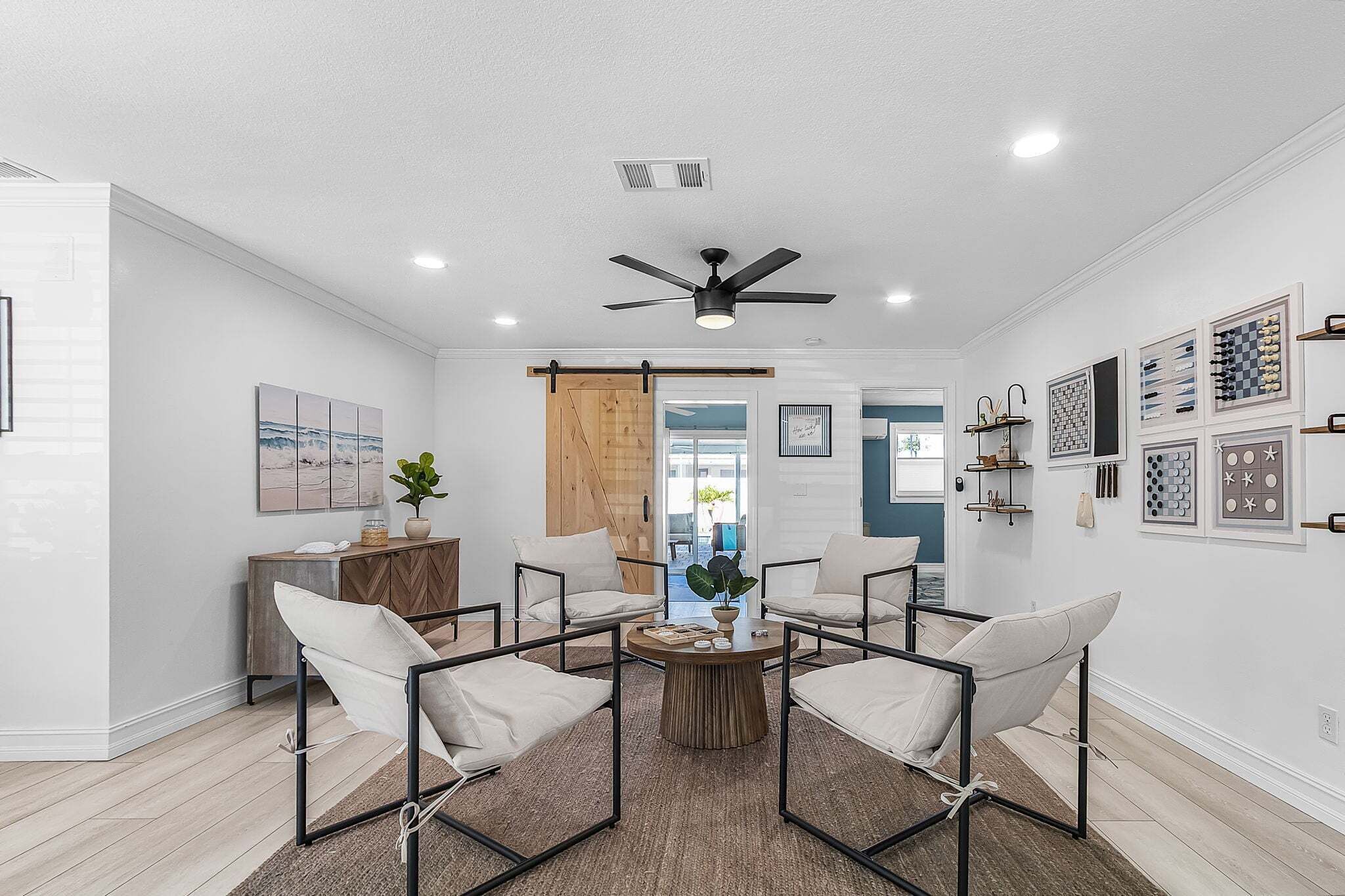 Un salon moderne avec un ventilateur de plafond, une table basse en bois et des fauteuils blancs.