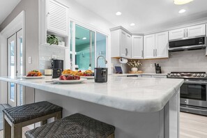 A modern kitchen with white cabinets, a large island, stainless steel appliances, and a glass door window. - Resort-Style Lanai Living with Pool, Spa & Outdoor Kitchen Fun - Lanai Life - Roelens (Cape Coral)