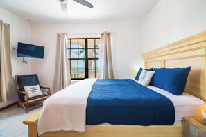 A bedroom with a bed, a chair, a TV, and a window with curtains.