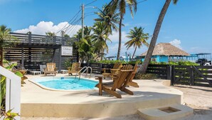 Un área de piscina con sillas de madera, un jacuzzi y palmeras.