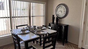 Un coin repas doté d’un parquet en bois disposé en chevrons, une table à manger mise avec des assiettes, des tasses et une horloge au mur.