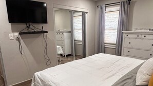 Une chambre à coucher comprenant un lit, un téléviseur à écran plat, un ventilateur de plafond, une commode et une fenêtre avec des rideaux.