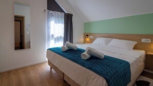 Een hotelkamer met een bed, nachtkastje, spiegel, raam met gordijnen en een houten vloer.
