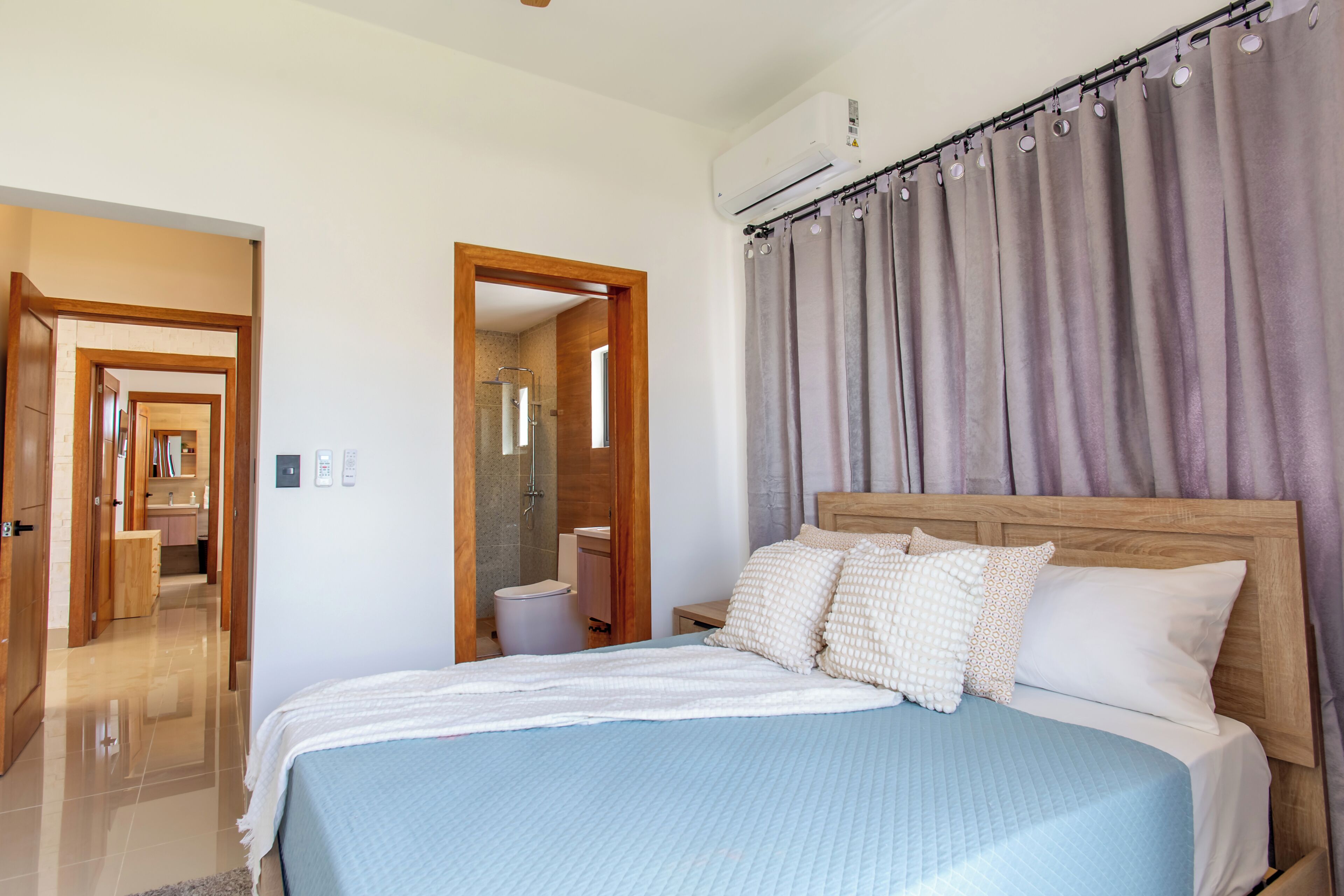 A bedroom with a bed, wooden headboard, and a bathroom visible through an open door.