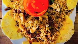Un plato de biryani con trozos de piña, huevos cocidos y una guarnición de salsa.