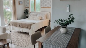 A bedroom with a bed, bedside table, chairs, a window, and a painting on the wall. - Pet Friendly Studio / Walk to Beach & Eats (Panama City Beach)