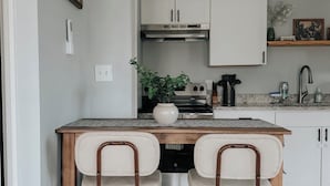 A kitchen with white cabinets, a wooden table, two chairs, a plant, and a stove. - Pet Friendly Studio / Walk to Beach & Eats (Panama City Beach)