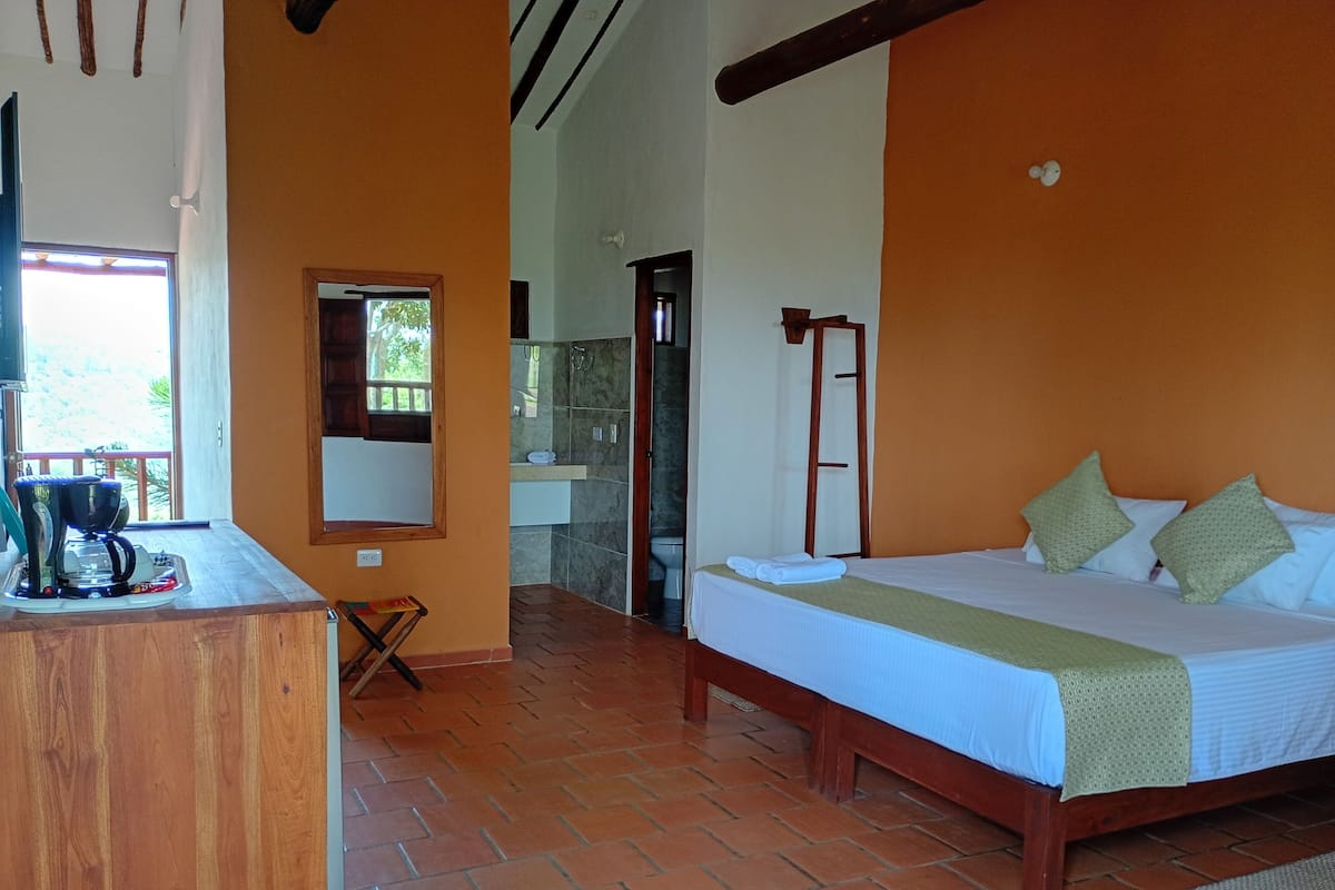 A room with a bed, a wooden desk, a mirror, and a bathroom visible through an open door.