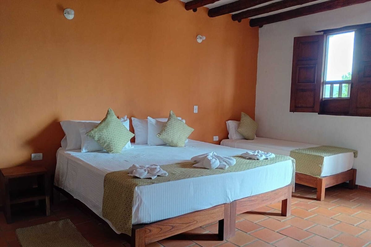 A double bed with a wooden frame, two bedside tables, a window with wooden shutters, and a tiled floor.