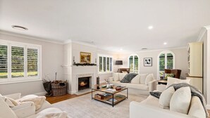 Un salon spacieux avec une cheminée, des meubles blancs et de grandes fenêtres.