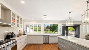 Une cuisine moderne dotée d’un grand îlot central, de meubles de rangement intégrés, d’une cuisinière et offrant une vue sur l’extérieur.