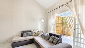 A modern living room with a sectional sofa, a floor lamp, and a view of a stone wall and plants outside.