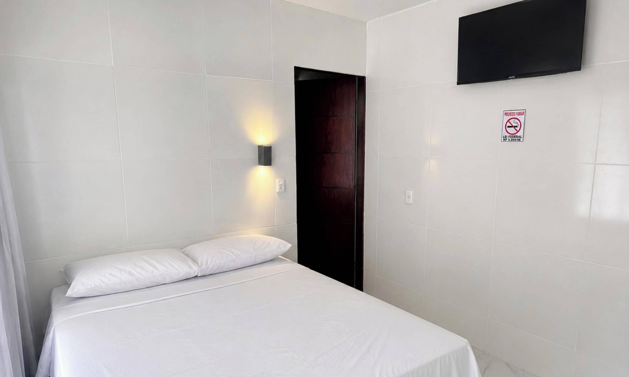 Quarto de hotel com cama, televisão na parede e porta.