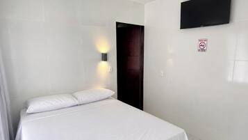 Quarto de hotel com cama, televisão na parede e porta.
