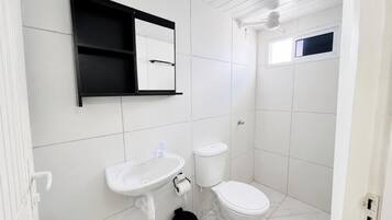 Un baño con lavamanos blanco, inodoro y espejo sobre el lavamanos.
