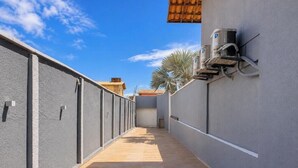 Un pasillo estrecho con suelo de baldosas, paredes grises y un cielo azul despejado.