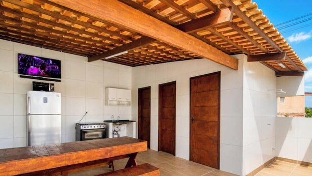 Una cocina con una mesa de madera, un refrigerador y una estufa. Hay tres puertas de madera y un televisor montado en la pared.