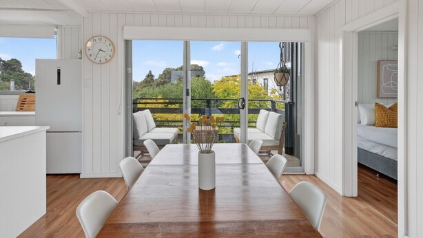 A modern kitchen with a wooden table and chairs, a dining area with a view of the outdoors, and a cozy bedroom with a bed and pillows. - Seventy at Yellow Doors (Goolwa South)