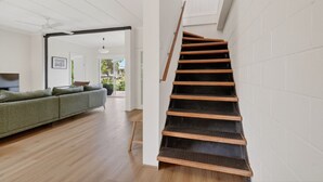 A staircase with wooden steps leading to a landing, a green sofa in a living area, and a view through a glass door to the outdoors. - Seventy at Yellow Doors (Goolwa South)