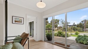 A modern interior with a wooden floor, a glass door leading to a garden, and a framed picture on the wall. - Seventy at Yellow Doors (Goolwa South)