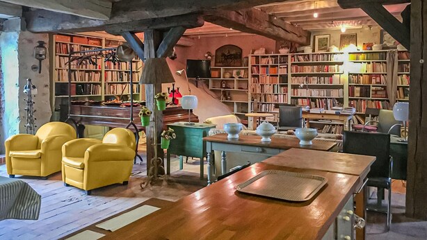 Een gezellige leeshoek met boekenkasten, een houten tafel en gele stoelen.