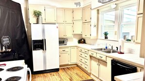 Una cocina con armarios blancos, un refrigerador, una estufa, un lavavajillas y una ventana con vistas.