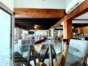 Ein modernes Wohnzimmer mit Glastisch, Sofas und einer Holzbalkendecke.
