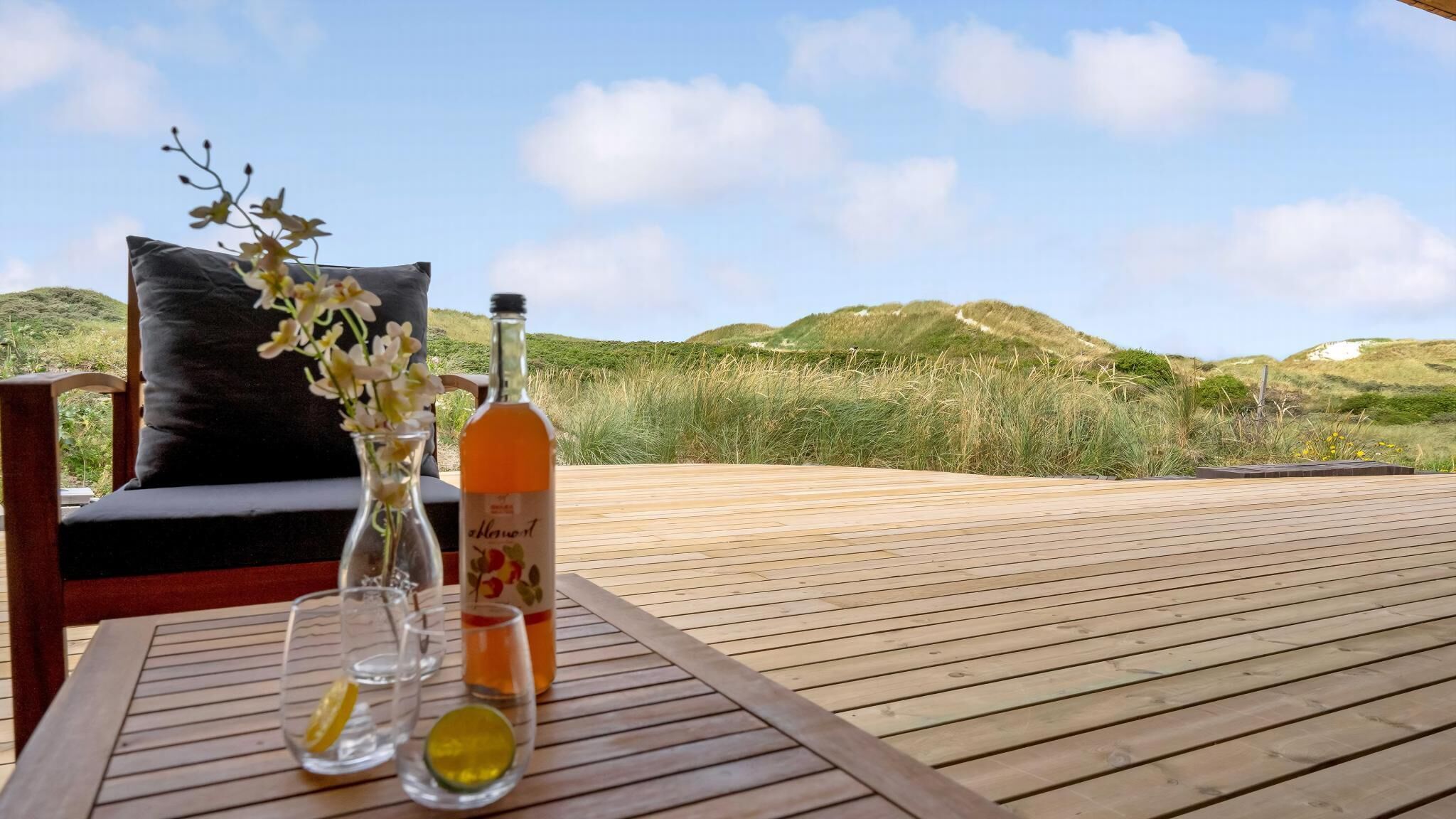 Een houten terras met drank, glazen en een bloevas.