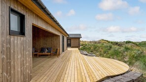 Een houten gebouw met terras, buitenmeubels en uitzicht op het omliggende landschap.