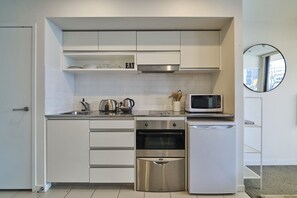 A compact kitchen with white cabinetry, a stainless steel oven, a microwave, and a small sink. - Cosy 1 Bed Apartment in Lighter Quay with Parking (Auckland City)
