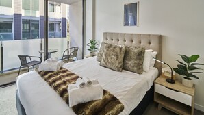Hotellihuone, jossa on suuri sänky, näköala kaupunkiin, pieni pöytä ja tuoli.