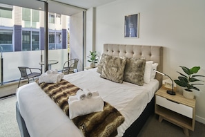 A hotel room with a large bed, a view of the city, a small table, and a chair. - Cosy 1 Bed Apartment in Lighter Quay with Parking (Auckland City)