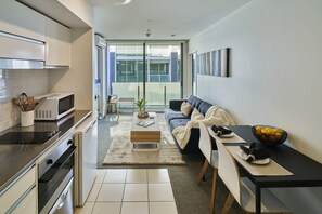 A modern kitchen with a microwave, stove, and oven. There is a dining area with a sofa and a table, and a large window providing a view of the outside. - Cosy 1 Bed Apartment in Lighter Quay with Parking (Auckland City)
