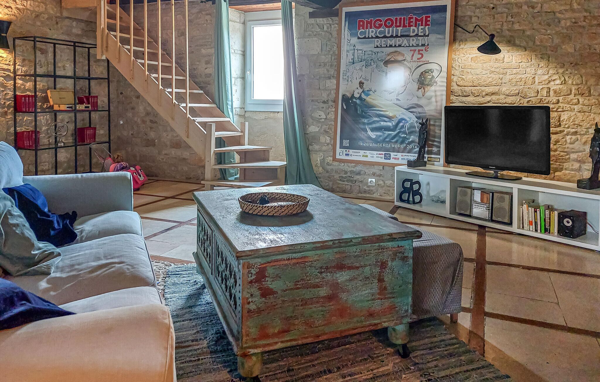 Un salon chaleureux avec un escalier, une affiche ancienne, un téléviseur et une bibliothèque.