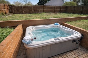 A hot tub with a control panel, a towel, and two glasses of red wine.